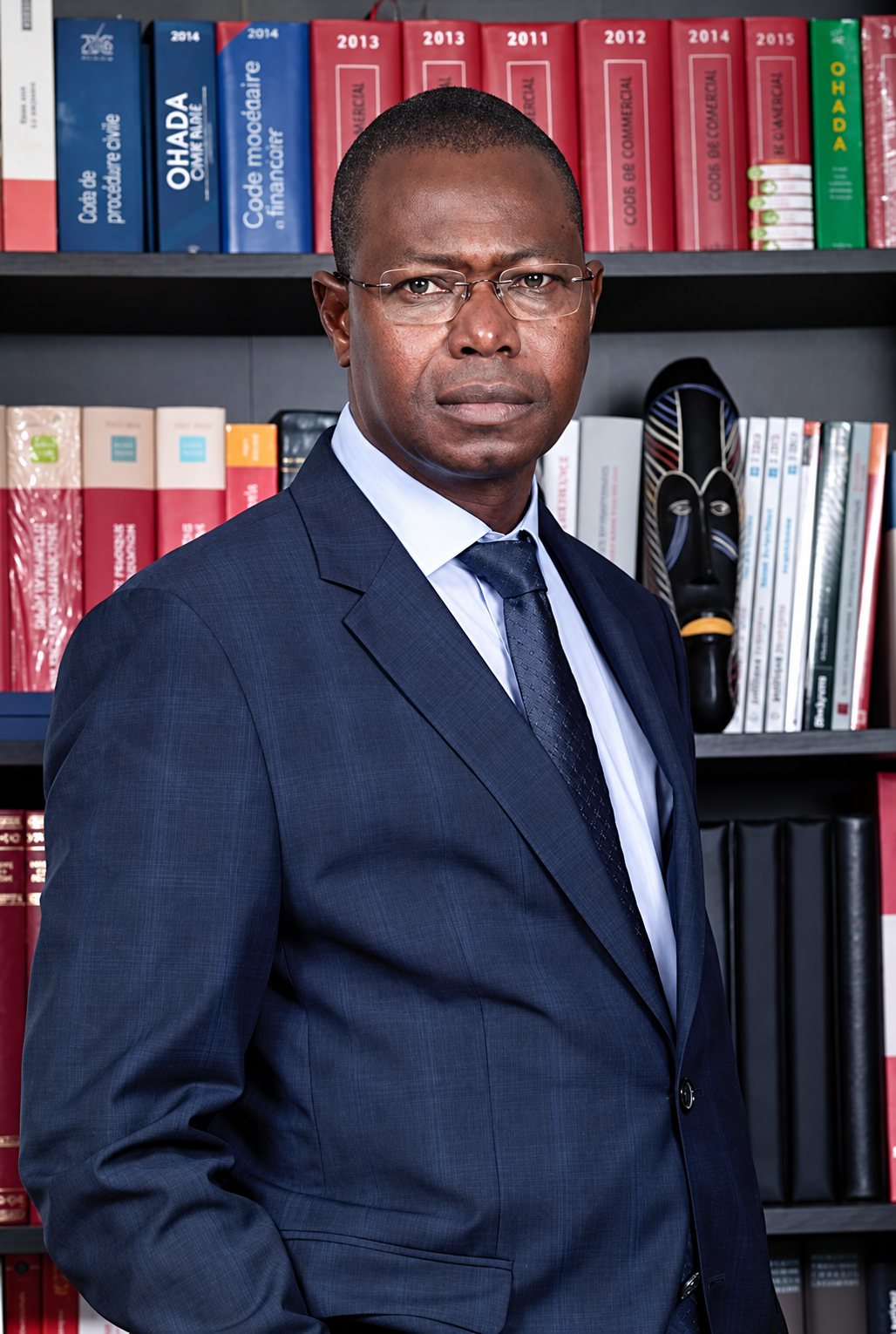 Maître Issaka ZAMPALIGRE, en costume, debout devant une bibliothèque juridique